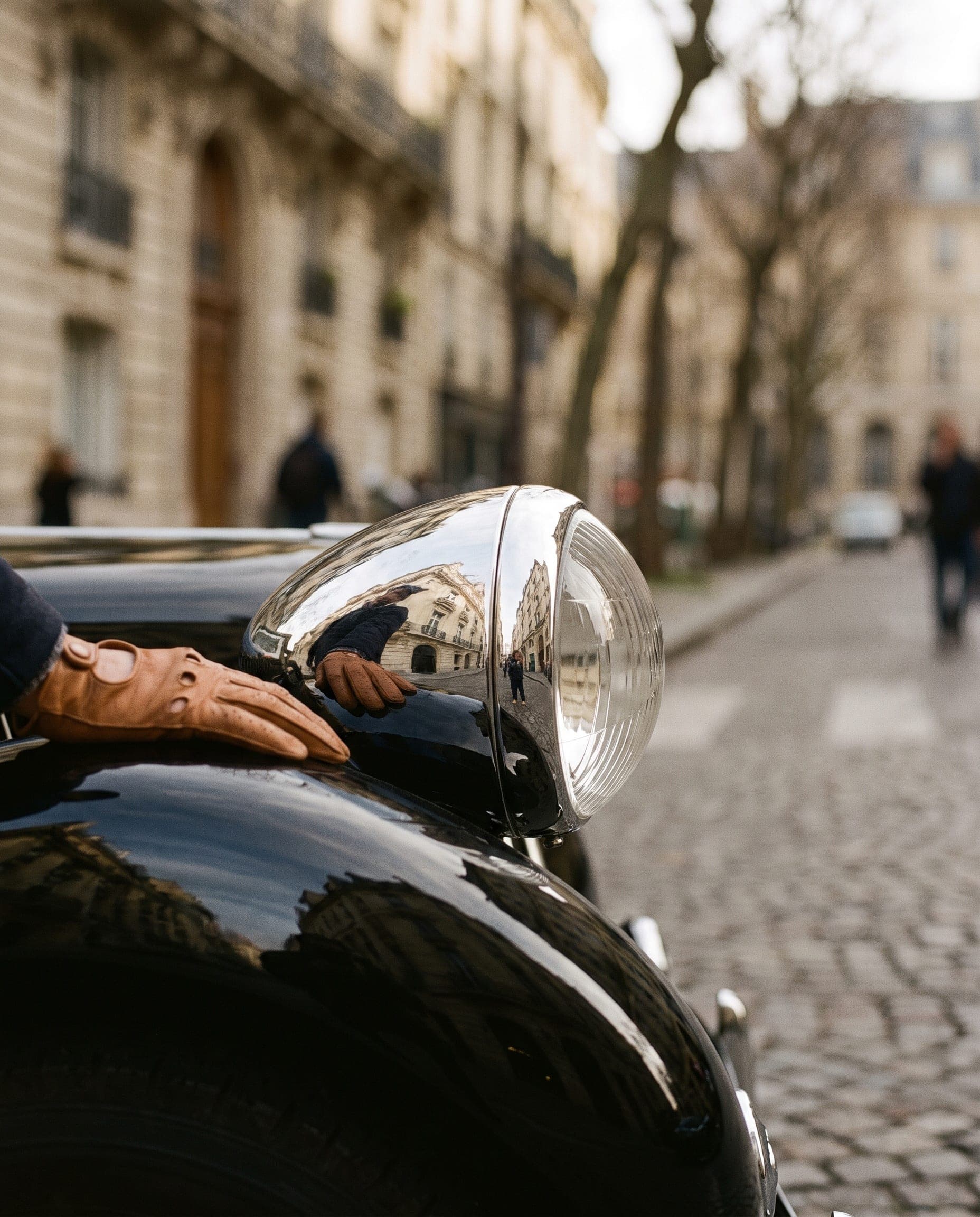 A gloved hand resting on the chrome headlamp of a black Citroën Traction Avant